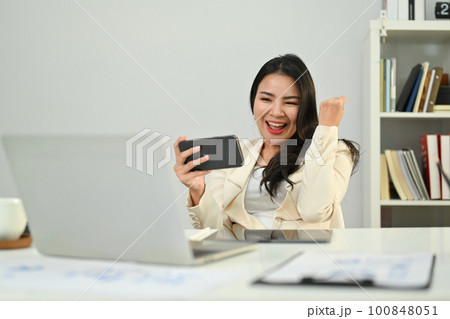 Overjoyed asian woman worker looking at mobile phone and celebrating success, excited by good news in email or message Overjoyed asian woman worker looking at mobile phone and celebrating success, excited by good news in email or message 100848051