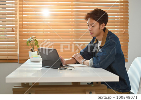 Young asian man in jeans jacket using digital tablet at home. Freelance, distance, education, e-learning concept 100848071
