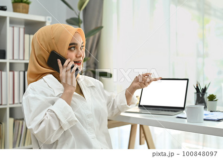 Portrait of muslim woman in hijab having pleasant phone conversation, enjoying mobile communication at office 100848097