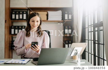 Confident business expert attractive smiling young woman typing laptop ang holding digital tablet on desk in office. Confident business expert attractive smiling young woman typing laptop ang holding digital tablet on desk in office. 100848358
