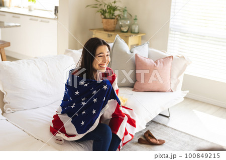 Excited caucasian young woman with flag of america watching match while sitting on sofa at home Excited caucasian young woman with flag of america watching match while sitting on sofa at home 100849215