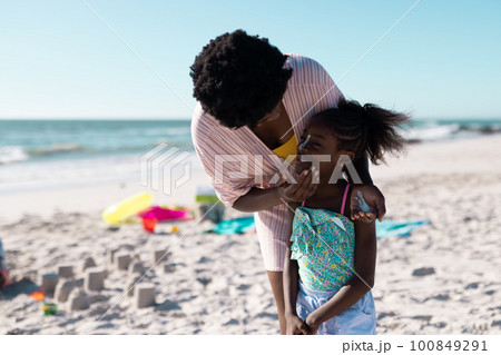 African american mother applying sunscreen on daughter's face at beach against clear sky, copy space African american mother applying sunscreen on daughter's face at beach against clear sky, copy space 100849291