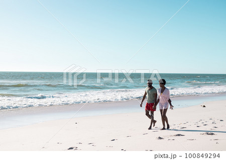 African american mid adult couple talking and walking on sandy beach against beautiful sea and sky 100849294