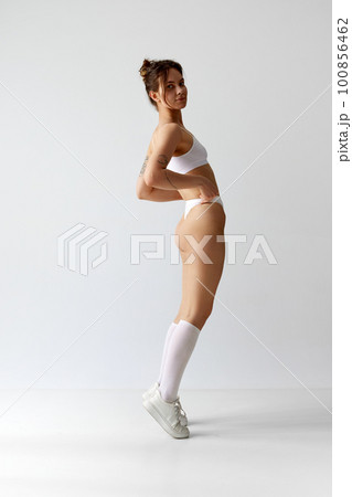 Full-length portrait of young girl with slim, fit body in underwear, high socks and sneakers against grey studio background. On tiptoe Full-length portrait of young girl with slim, fit body in underwear, high socks and sneakers against grey studio background. On tiptoe 100856462
