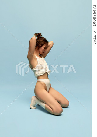 Portrait of young girl with slim body, in underwear and socks posing against blue studio background. Body-positivity 100856473