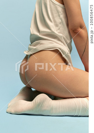 Cropped image of female body, buttocks. Model in t-shirt, socks and underwear posing against blue studio background. Cropped image of female body, buttocks. Model in t-shirt, socks and underwear posing against blue studio background. 100856475