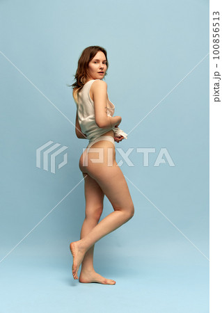 Full-length image of slim, beautiful, young girl in comfortable homewear posing against blue studio background. Anti-cellulite care Full-length image of slim, beautiful, young girl in comfortable homewear posing against blue studio background. Anti-cellulite care 100856513