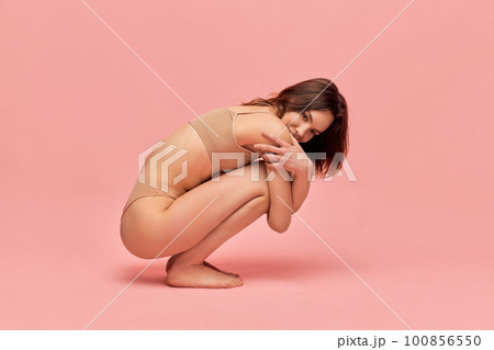Tender femininity. Portrait of attractive, cute, young girl in beige underwear posing against pink studio background. Tender femininity. Portrait of attractive, cute, young girl in beige underwear posing against pink studio background. 100856550
