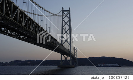 兵庫県立舞子公園から見た夕暮れの明石海峡大橋、橋の下を通過した名門大洋フェリーのフェリー 兵庫県立舞子公園から見た夕暮れの明石海峡大橋、橋の下を通過した名門大洋フェリーのフェリー 100857425