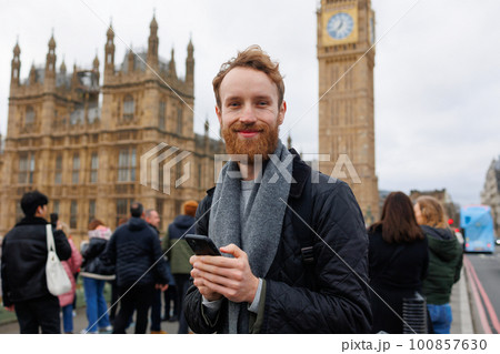 Portrait of a happy man with a smartphone in his hands standing on the Westminster Bridge against the backdrop of Big Ben tower 100857630