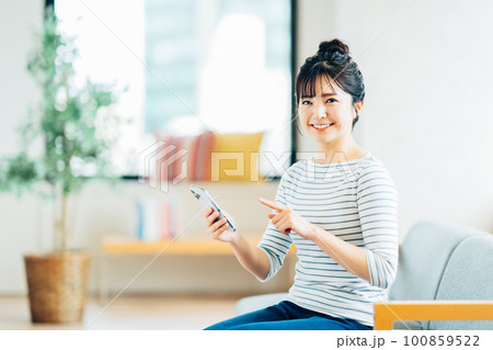 リビングでスマホを見る若い女性 100859522
