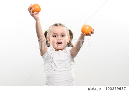 Portrait of a small beautiful girl on a white background with tangerines in her hands. 100859627