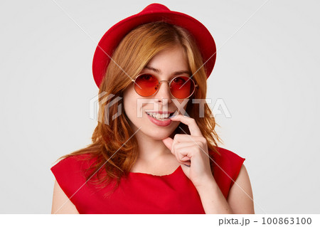 Glamour attractive young female keeps finger near mouth, smiles broadly, shows white teeth, dressed in red clothes, wears stylish sunglasses, being in high spirit after celebrating her birthday Glamour attractive young female keeps finger near mouth, smiles broadly, shows white teeth, dressed in red clothes, wears stylish sunglasses, being in high spirit after celebrating her birthday 100863100