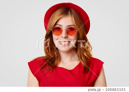 Horizontal shot of happy European female with sincere smile, wears everything in red colour, has fashionable style, glad after making new purchase, isolated over white background. Fashion concept Horizontal shot of happy European female with sincere smile, wears everything in red colour, has fashionable style, glad after making new purchase, isolated over white background. Fashion concept 100863101