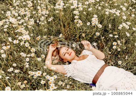 A woman lies in a chamomile field, dressed in a white dress A woman lies in a chamomile field, dressed in a white dress 100865044