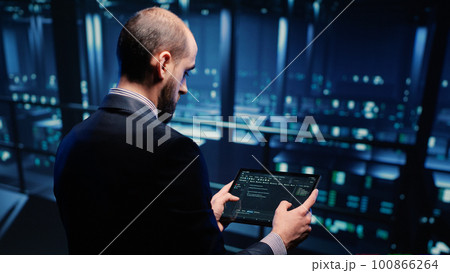 IT support specialist working with hosting server using tablet in professional data center, planning web digitalization. Male database admin inspecting system hardware in networking industry. 100866264