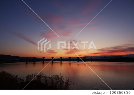 赤く朝焼けした空と映り込む川・春・230301am 100866350