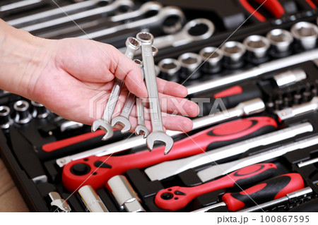 Tool store. Closeup of male hand holding wrenches. Auto repair kit in toolbox. Repairman instruments set. Inside the toolbox there are black-red wrenches, spanners and different nozzles. Closeup. 100867595