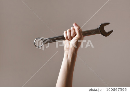 big spanner in the woman's hand. hand holds a wrench on a gray background. Combination wrench. big chrome vanadium spanner in the hand. women's work. labor day. 100867596