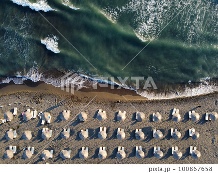 View from above, stunning aerial view of an amazing empty beach with white beach umbrellas and turquoise clear water with waves. 100867658