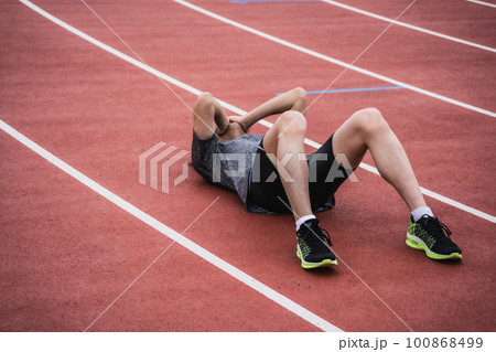 トラックで倒れ込み両手で顔を覆う男性ランナー 100868499