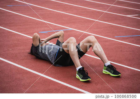 トラックで倒れ込み両手で顔を覆う男性ランナー 100868500