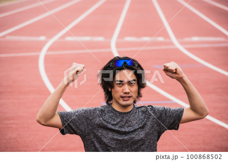 陸上競技のトラックでガッツポーズをする男性ランナー 100868502