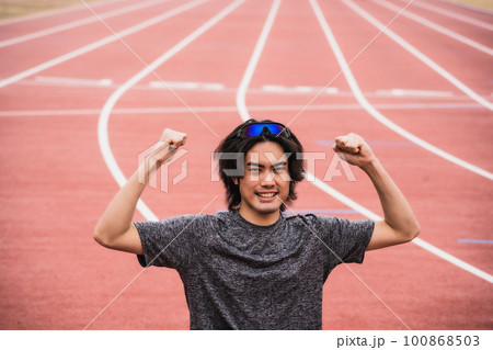 陸上競技のトラックでガッツポーズをする男性ランナー 100868503