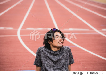 陸上競技のトラックに座り込む男性ランナー 100868505