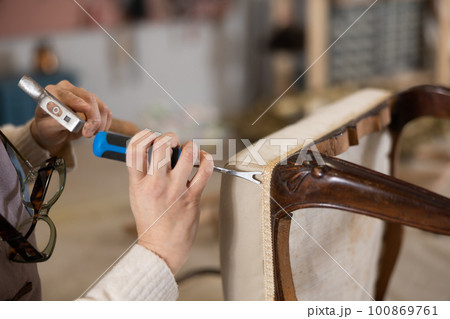 close up of hands of restorer reupholstering antique wooden chair with cabriole legs close up of hands of restorer reupholstering antique wooden chair with cabriole legs 100869761