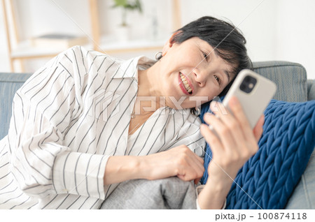 ソファーで寝転んでスマホを使う女性 100874118