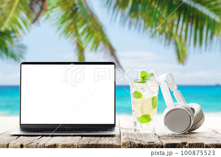 Laptop and headphones on wooden table in front of sunny sea Laptop and headphones on wooden table in front of sunny sea 100875523