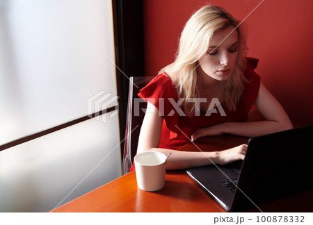 Young adult woman wearing red jumpsuit and using laptop 100878332