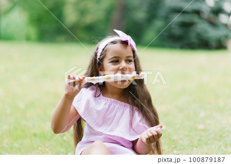 Cute baby girl in pink dress eats white cotton candy in the park in summer 100879187