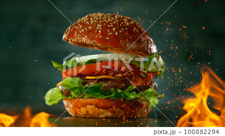 Tasty beef burger on black stone table with fire flames, close-up Tasty beef burger on black stone table with fire flames, close-up 100882294