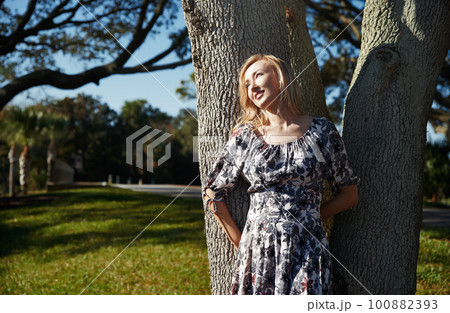 Beautiful woman leaning onto the oak tree 100882393