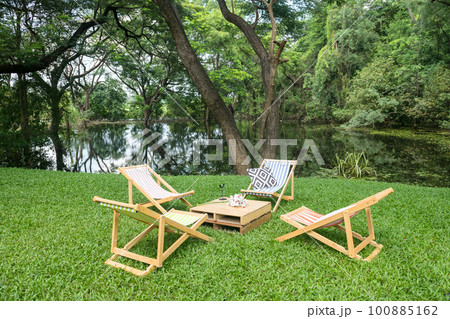 Sunbed chairs and table on green grass garden by pond 100885162