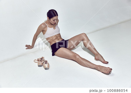 Tired ballerina sitting on floor and resting after hard work in dance hall over white background 100886054