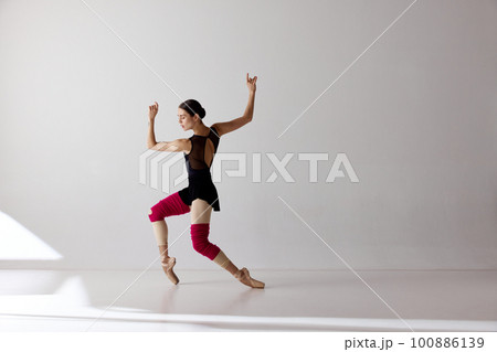 One young ballerina wearing pointe shoes dancing on fingertips over white background One young ballerina wearing pointe shoes dancing on fingertips over white background 100886139