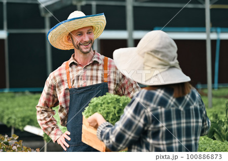 Portrait of happy farmer couple working in sunny hydroponic greenhouse. Agro cultivation and small business concept 100886873