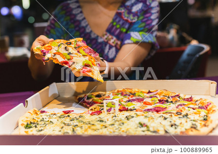 Woman hand taking a slice of New York pizza in takeaway box. Woman hand taking a slice of New York pizza in takeaway box. 100889965