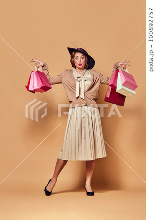 One charming woman wearing retro clothes holding paper bags over beige background. Sales, Black Friday concept 100892757