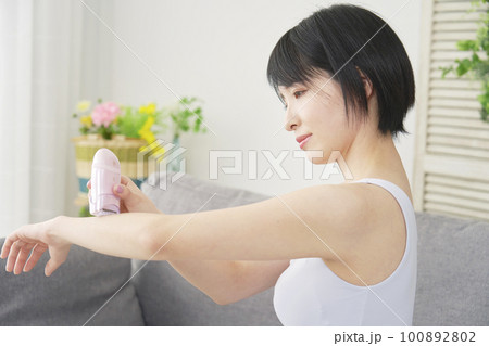 リビングで家庭用脱毛器で腕のセルフ脱毛をする女性 100892802