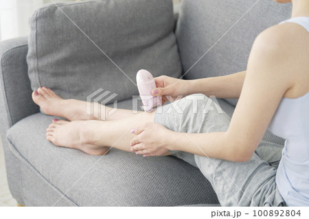 リビングで家庭用脱毛器で脚のセルフ脱毛をする女性　顔無し 100892804
