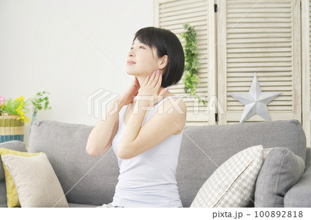 リビングで首元をセルフマッサージをする女性 100892818