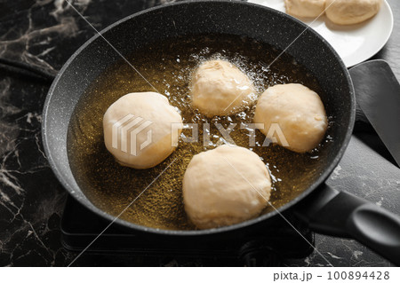 Cooking delicious donuts in hot oil, closeup 100894428