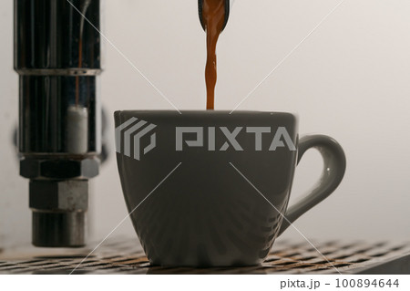 pulling espresso shot with single spout portafilter from coffee machine closeup 100894644