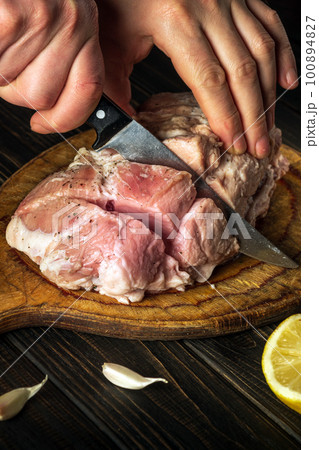 Professional chef cuts meat with a knife before baking. Spices on the kitchen table in a restaurant for preparing a delicious lunch or dinner. 100894827