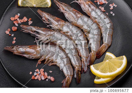 Tiger prawn or langoustine raw with spices and salt on a wooden cutting board Tiger prawn or langoustine raw with spices and salt on a wooden cutting board 100895677