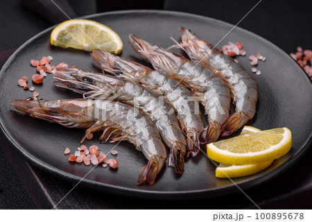 Tiger prawn or langoustine raw with spices and salt on a wooden cutting board Tiger prawn or langoustine raw with spices and salt on a wooden cutting board 100895678